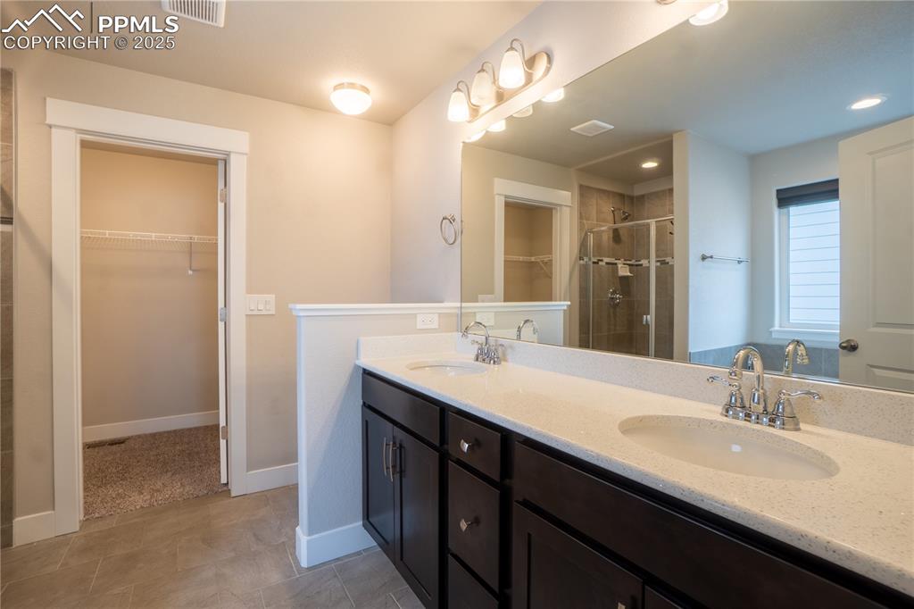 Image 21 of 35: Full bathroom with a spacious closet, a shower stall, double vanity, and li