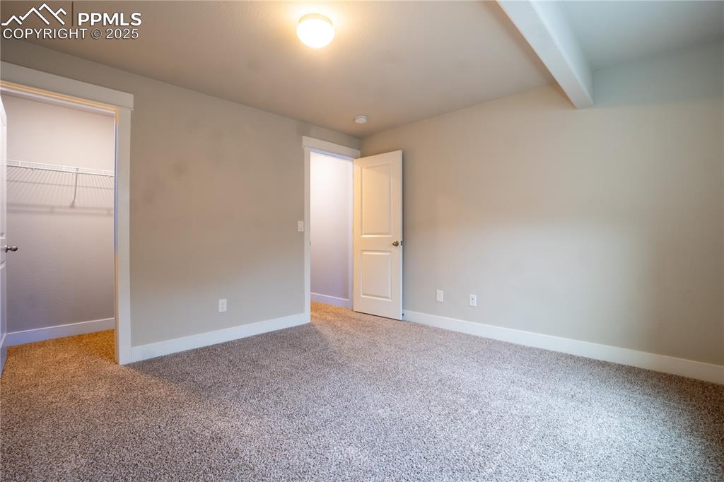 Image 31 of 35: Unfurnished bedroom with a spacious closet, beamed ceiling, and carpet floo