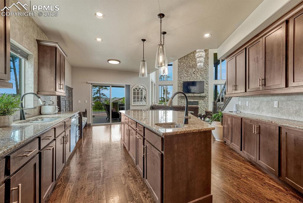 Image 10 of 50: Kitchen with a sink, a kitchen island with sink, a stone fireplace, decorat
