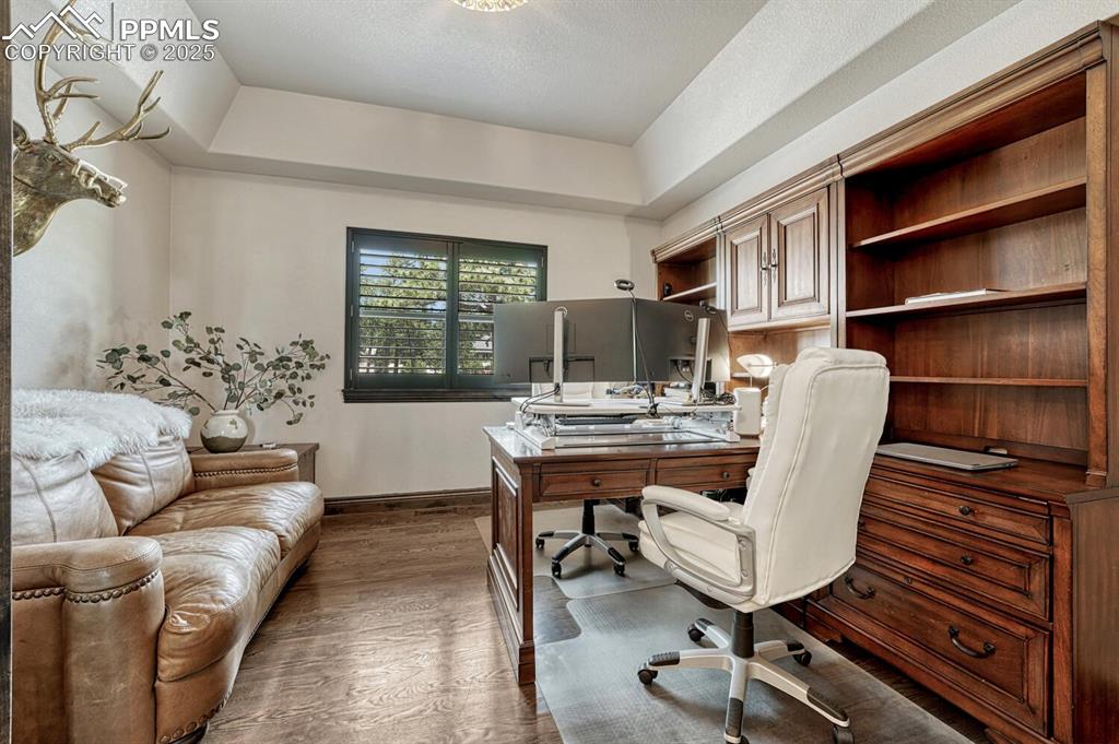 Image 16 of 50: Office area with dark wood-style flooring, baseboards, and a raised ceiling