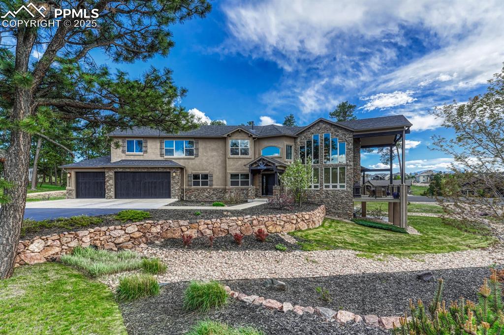 Image 2 of 50: View of front of house with stone siding, driveway, stucco siding, a garage