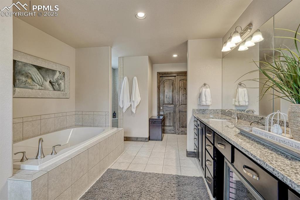 Image 29 of 50: Full bathroom with double vanity, tile patterned flooring, a bath, recessed
