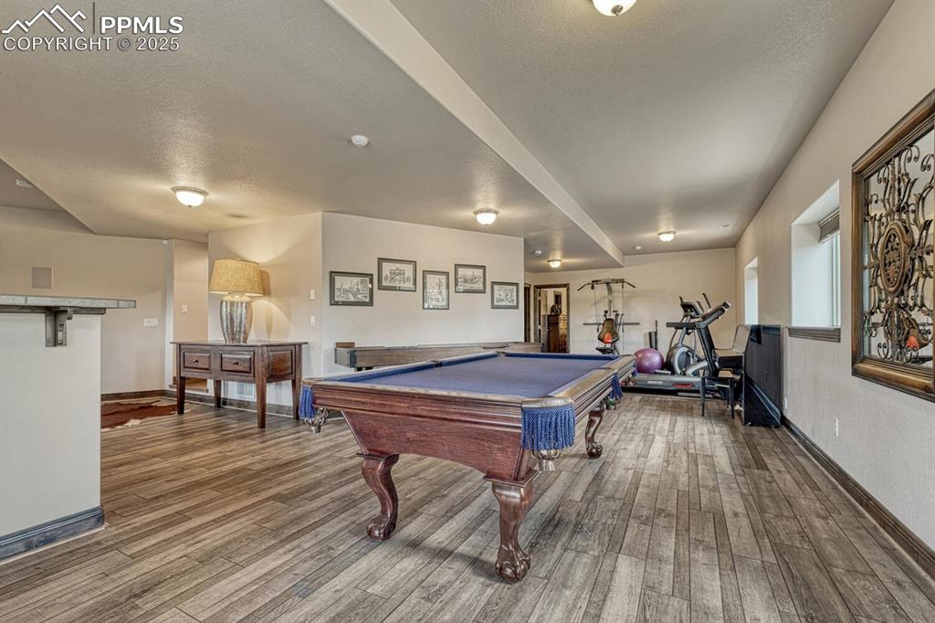 Image 34 of 50: Recreation room with wood finished floors, baseboards, billiards, and a tex