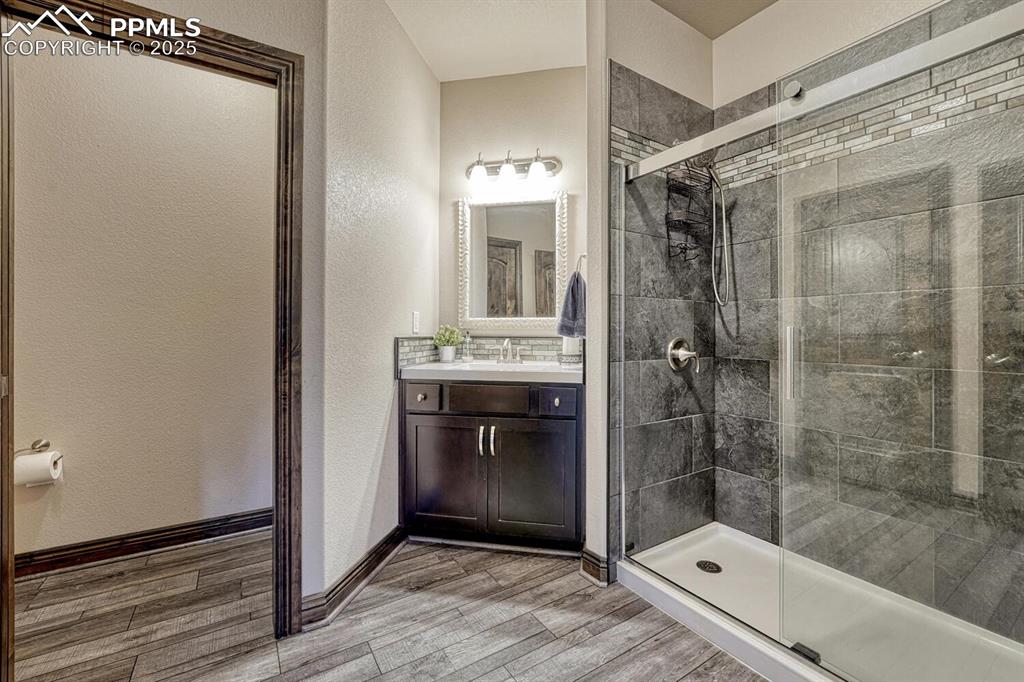 Image 38 of 50: Bathroom featuring a stall shower, a textured wall, vanity, wood finished f