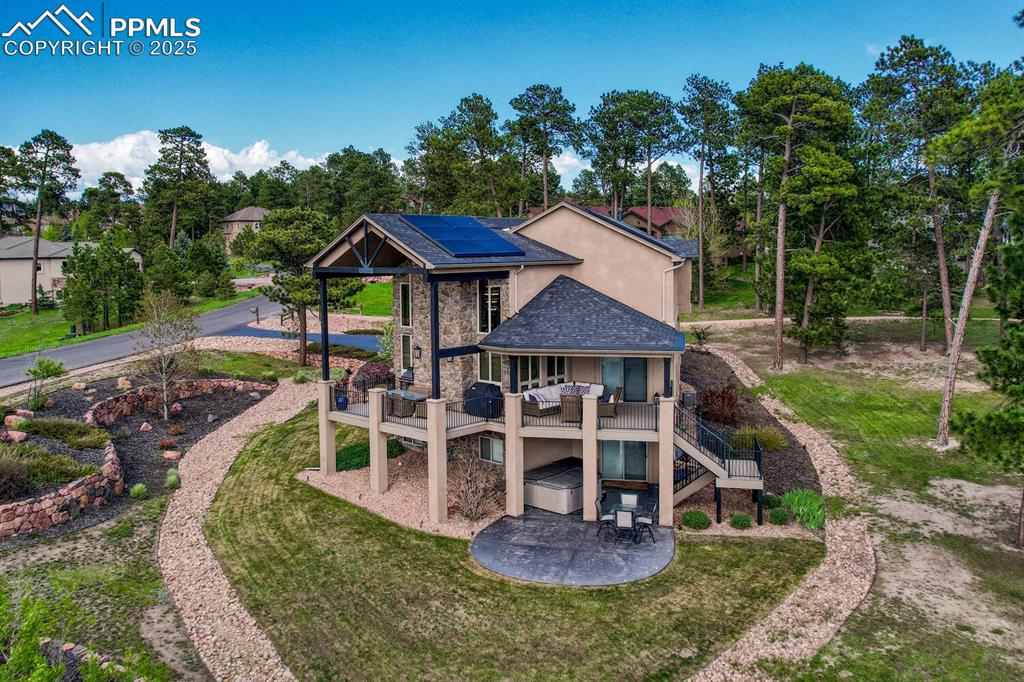 Image 47 of 50: Back of house featuring a patio, solar panels, a lawn, stone siding, and st