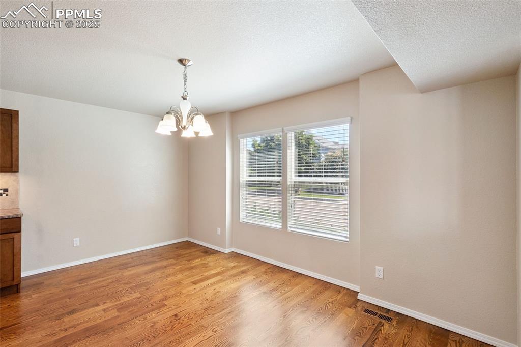 Image 12 of 30: Spare room featuring a chandelier, light wood finished floors, and a textur