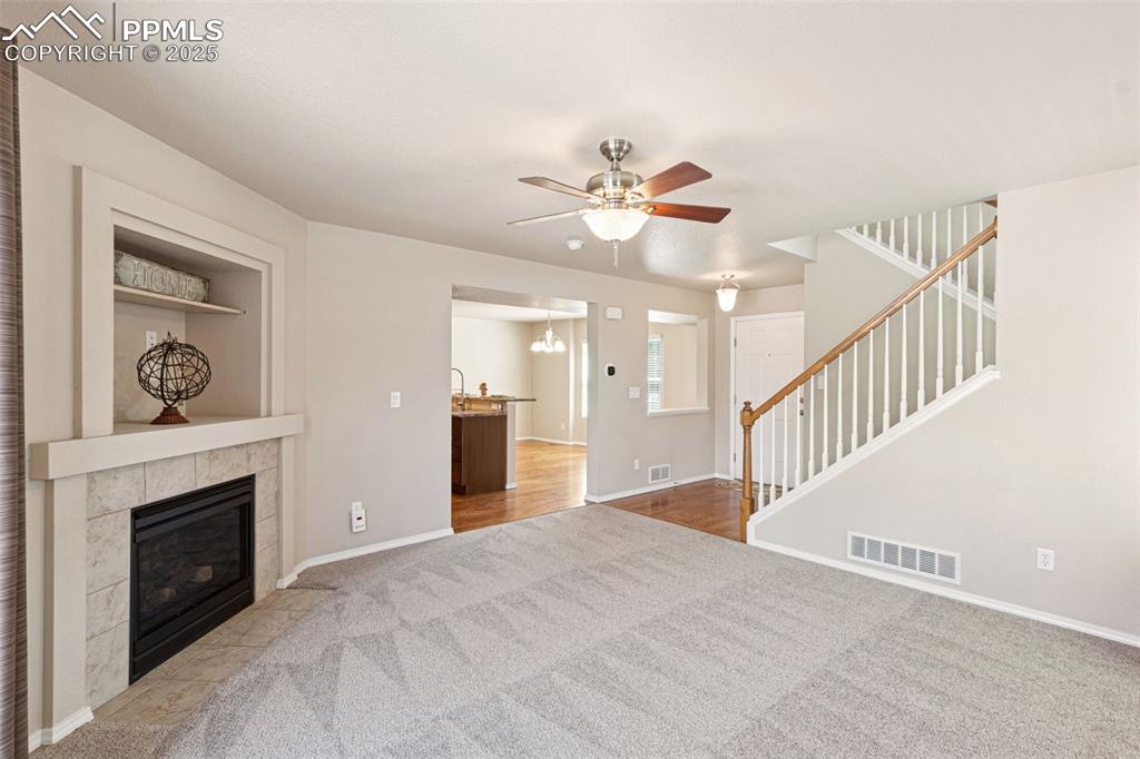Image 7 of 30: Unfurnished living room with carpet, ceiling fan, a tiled fireplace, and st
