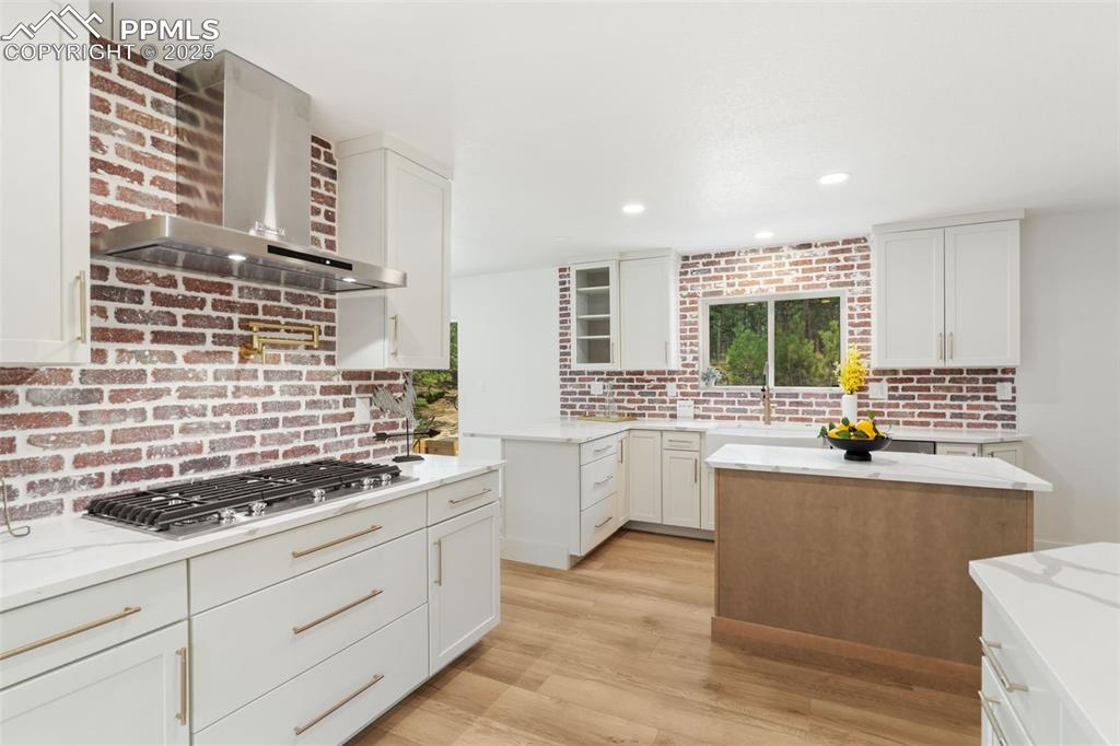 Image 12 of 43: Kitchen with white cabinets, wall chimney exhaust hood, light stone counter