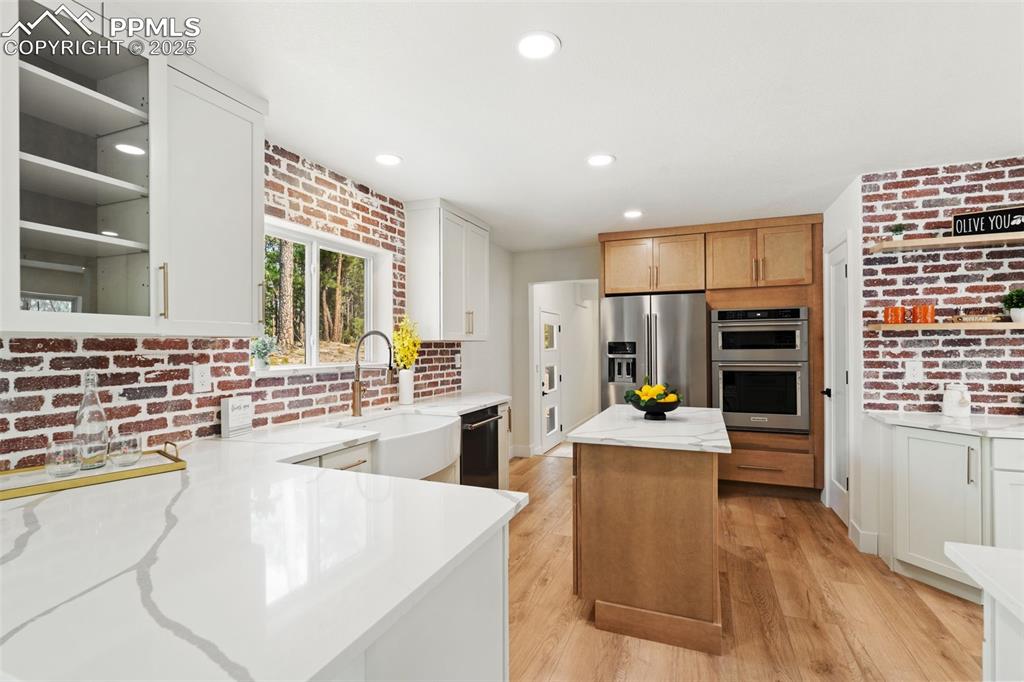 Image 14 of 43: Kitchen with brick wall, light stone countertops, a center island, light wo