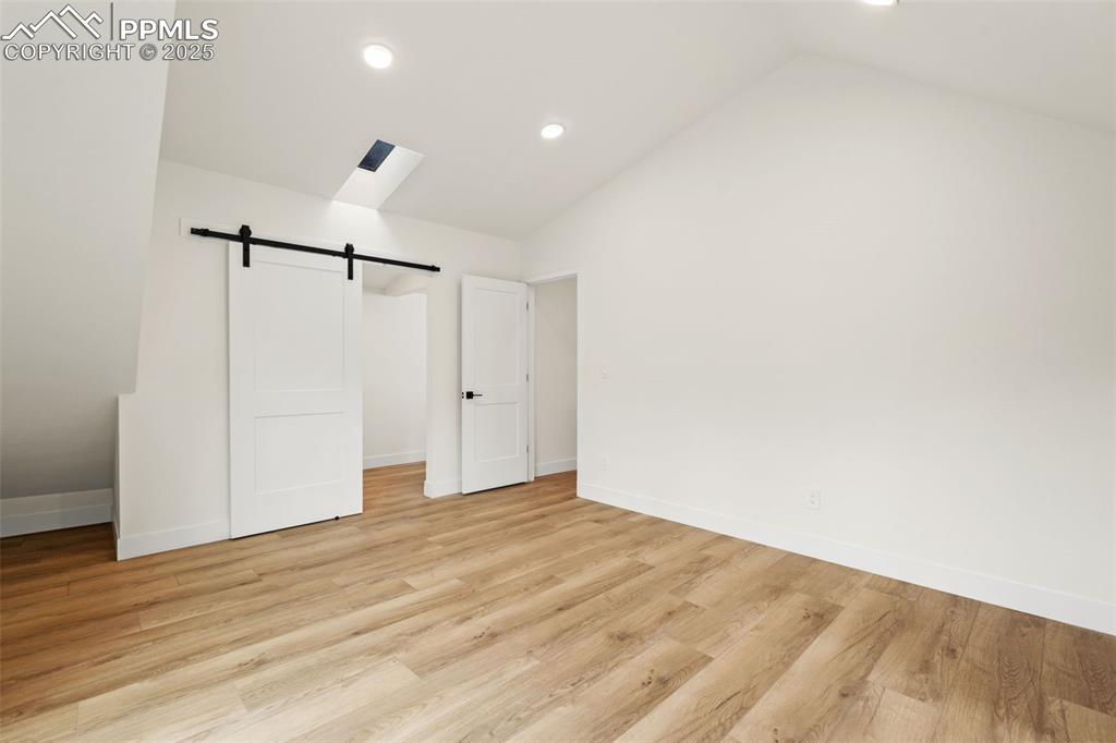 Image 21 of 43: Unfurnished bedroom featuring a barn door, vaulted ceiling, light wood fini