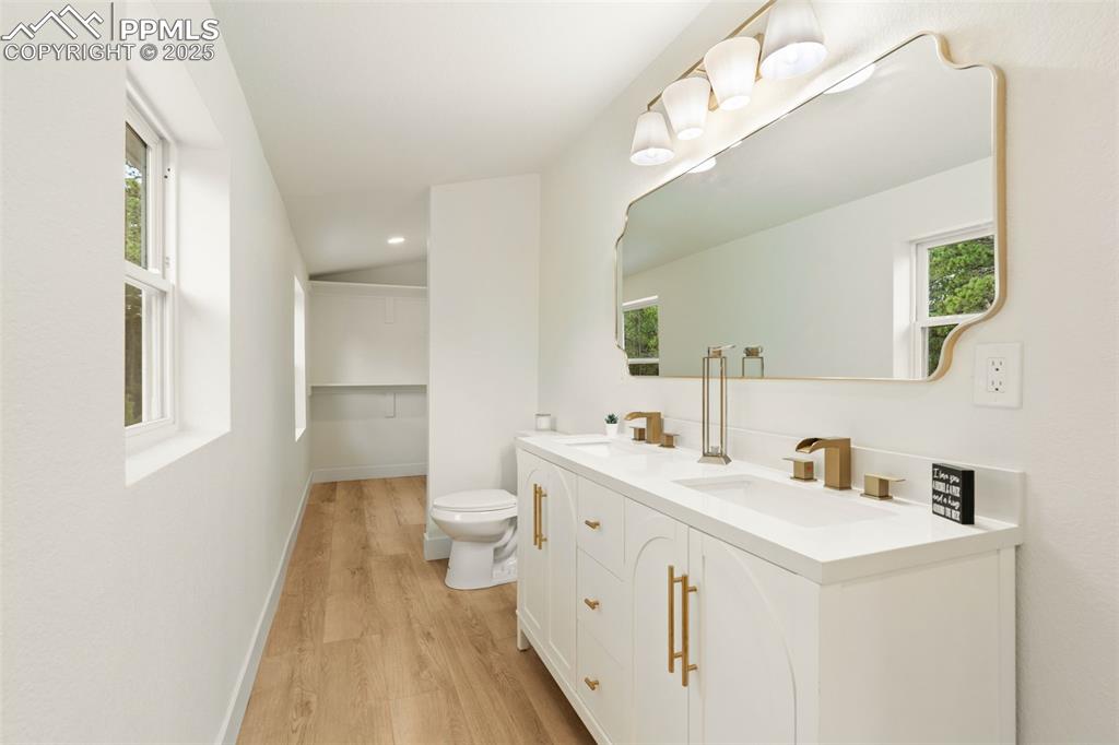 Image 22 of 43: Full bath with light wood finished floors, double vanity, lofted ceiling, a