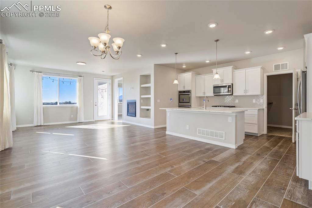 Image 39 of 44: Kitchen with white cabinetry, hanging light fixtures, built in shelves, ope