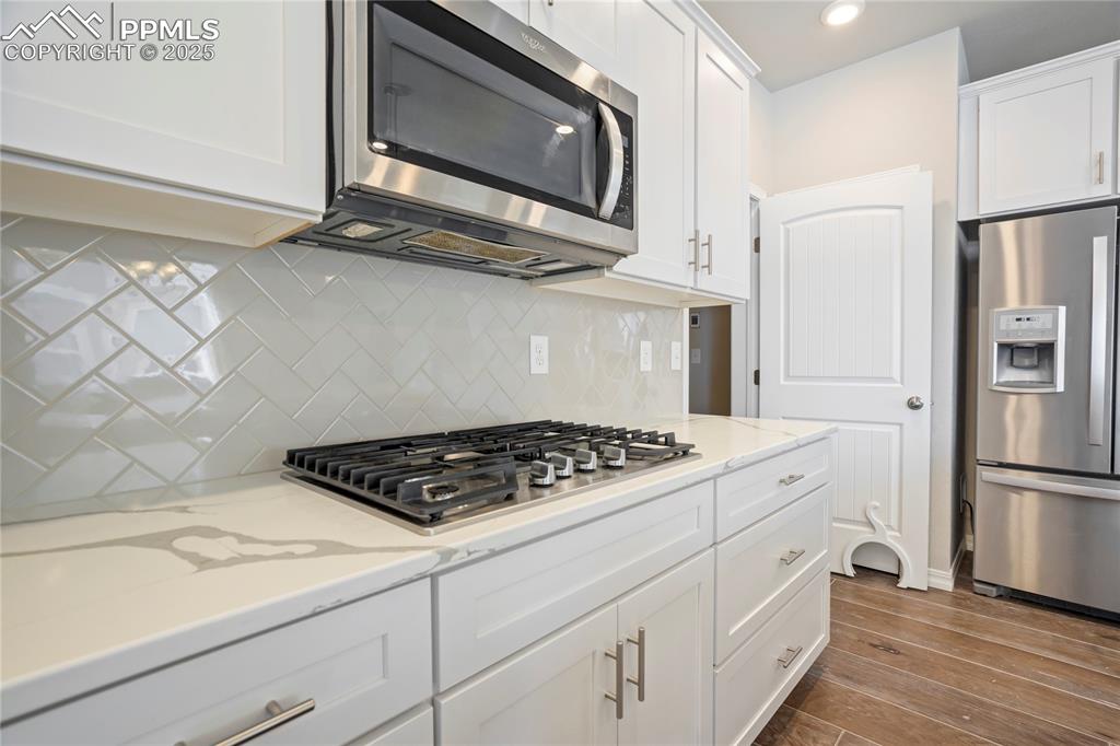 Image 7 of 44: Kitchen with stainless steel appliances, white cabinets, backsplash, dark w