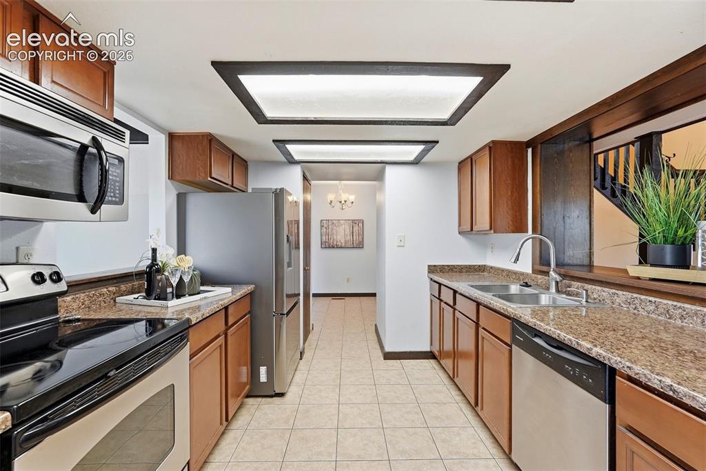 Image 12 of 50: Galley kitchen featuring wood cabinetry, stainless steel appliances, speckl