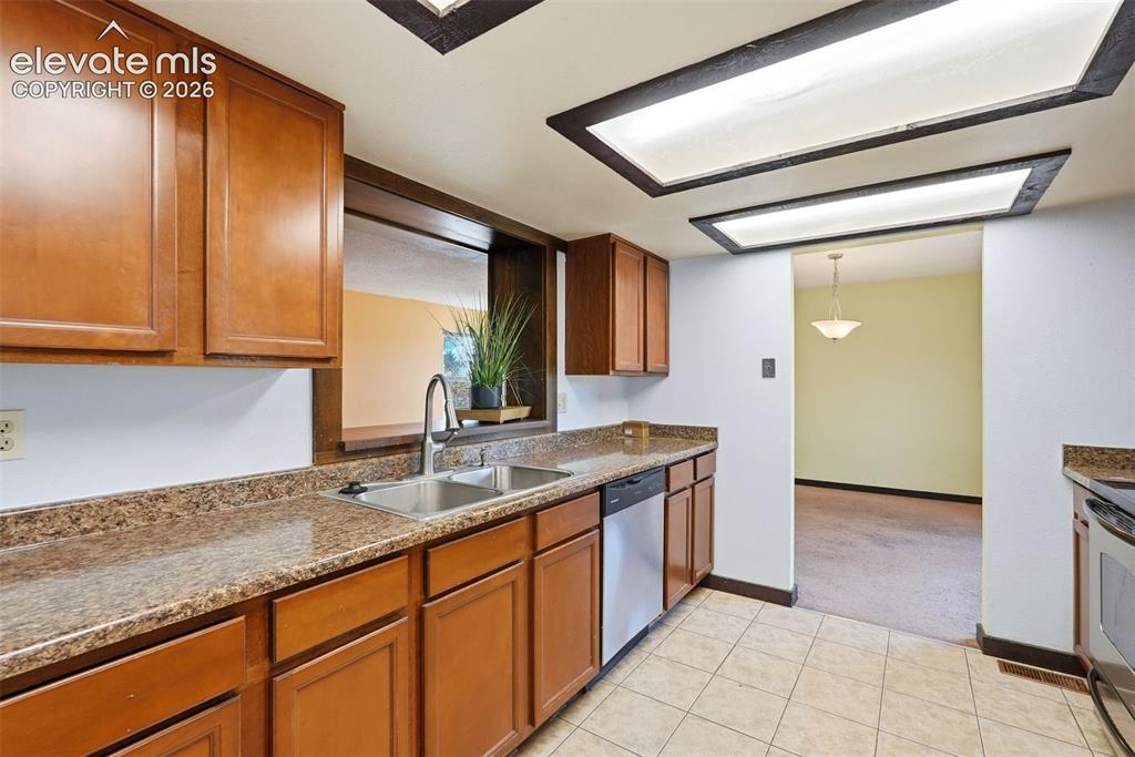 Image 13 of 50: Kitchen featuring wood cabinetry, speckled countertops, a double-basin stai