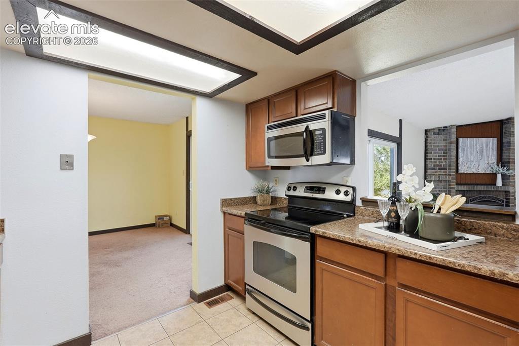 Image 14 of 50: Kitchen featuring tile flooring, wood-finish cabinetry, stainless steel app