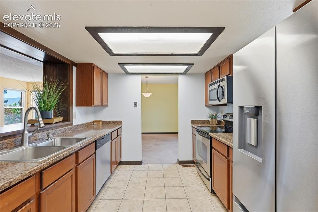 Image 15 of 50: Galley kitchen featuring wood cabinetry, stone-finish countertops, and stai