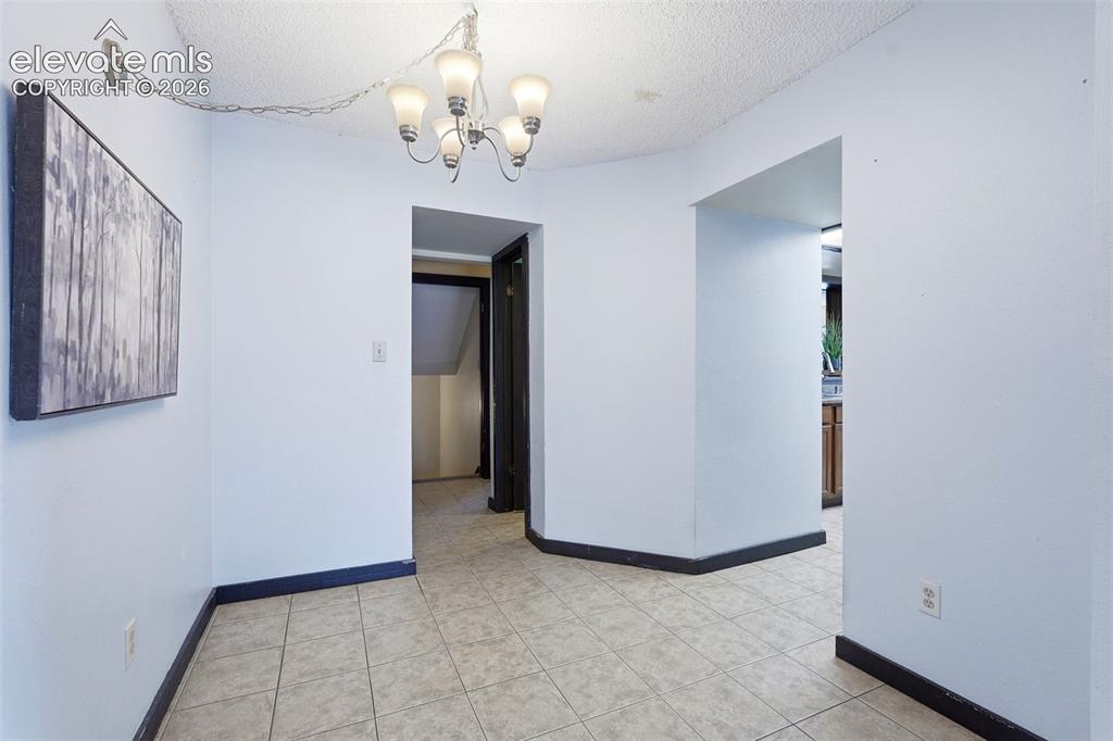 Image 16 of 50: Tiled flooring extends through this interior space with white walls and dar