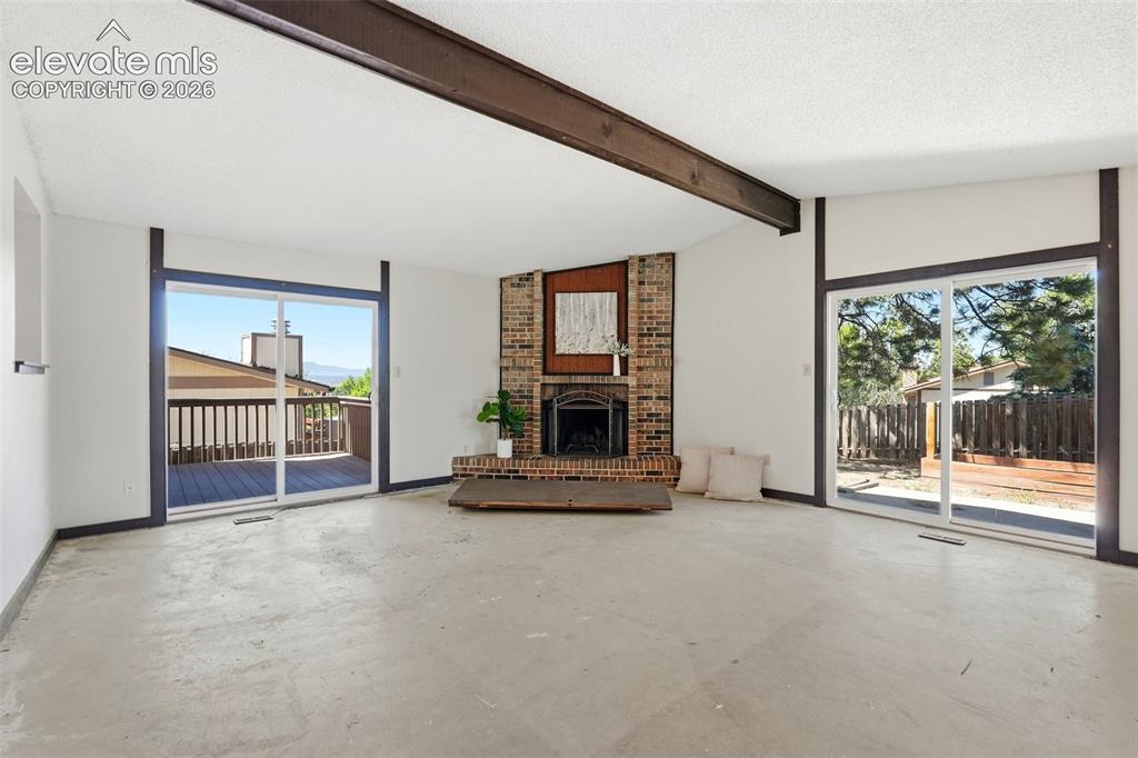 Image 18 of 50: Spacious living area featuring a brick fireplace, exposed wood beam, two la