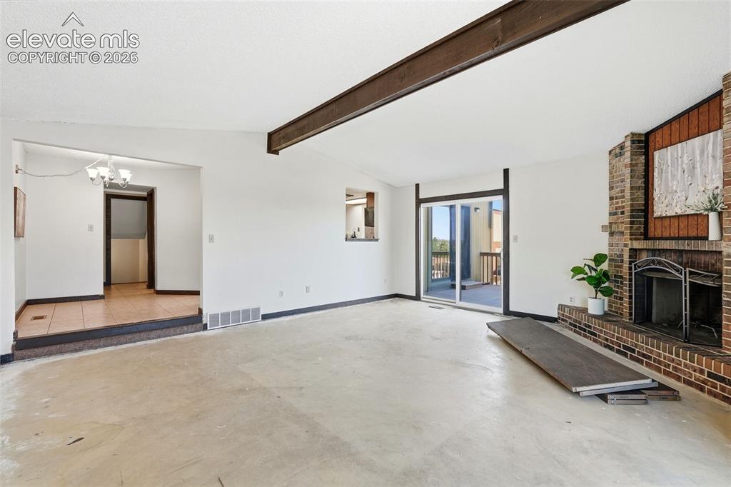 Image 19 of 50: Spacious living area featuring a prominent brick fireplace, exposed ceiling