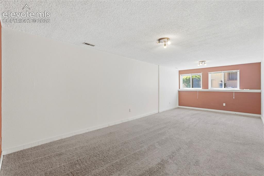 Image 21 of 50: Spacious room featuring neutral carpeting, white textured ceilings, and a l