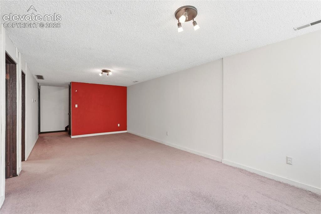 Image 23 of 50: Spacious room featuring light pink carpeting and white walls with one accen