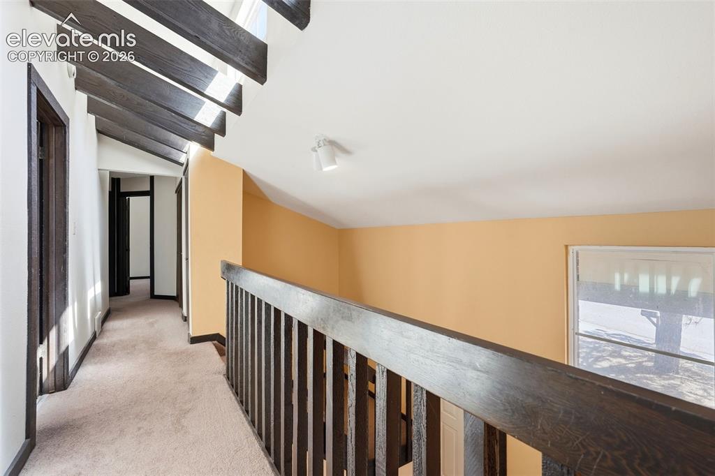 Image 32 of 50: Carpeted hallway with exposed dark wood beams and matching trim