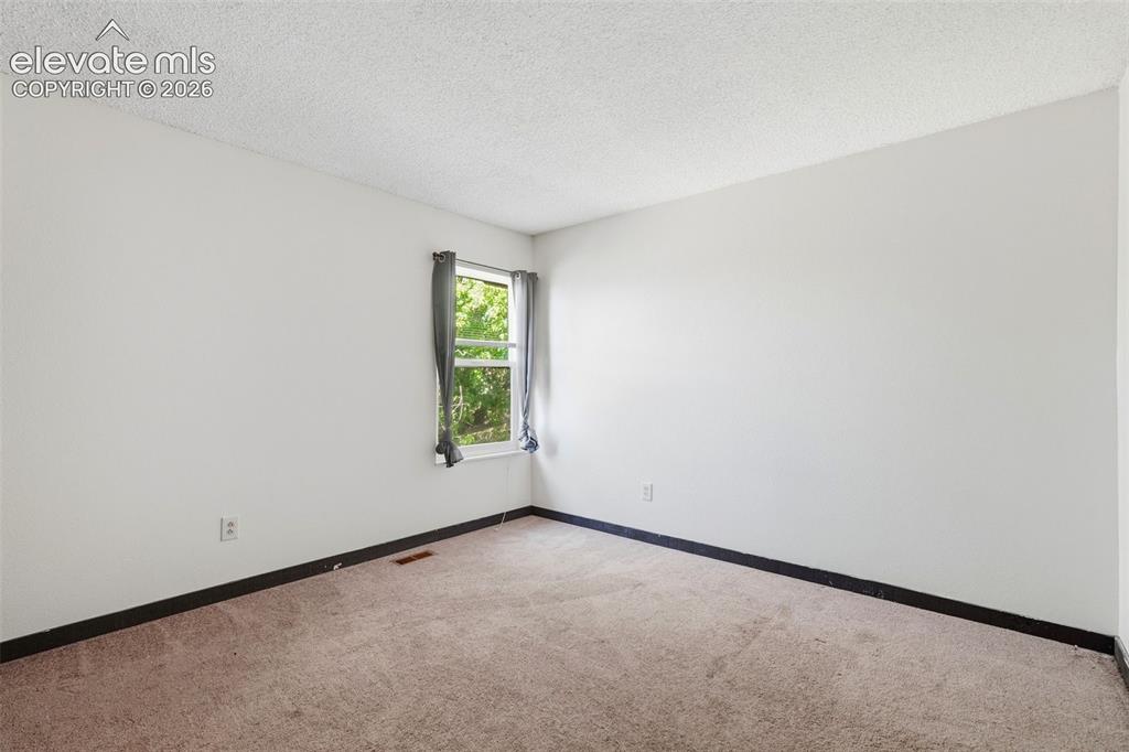 Image 38 of 50: Carpeted room featuring a single window with drapes, painted walls, and dar