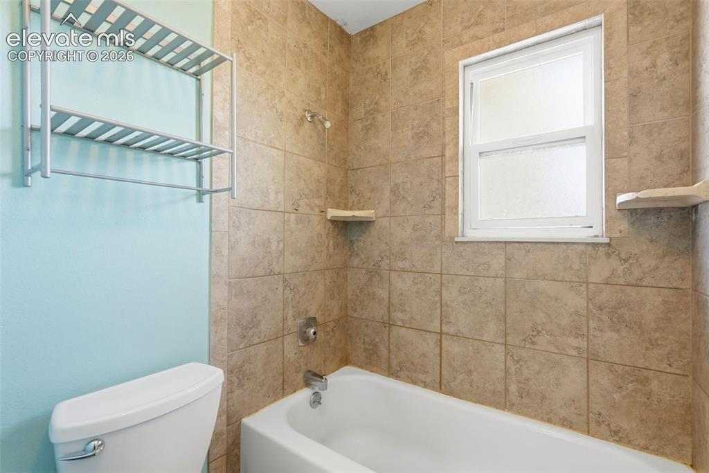 Image 40 of 50: Bathroom featuring a white porcelain tub, light brown ceramic tile surround