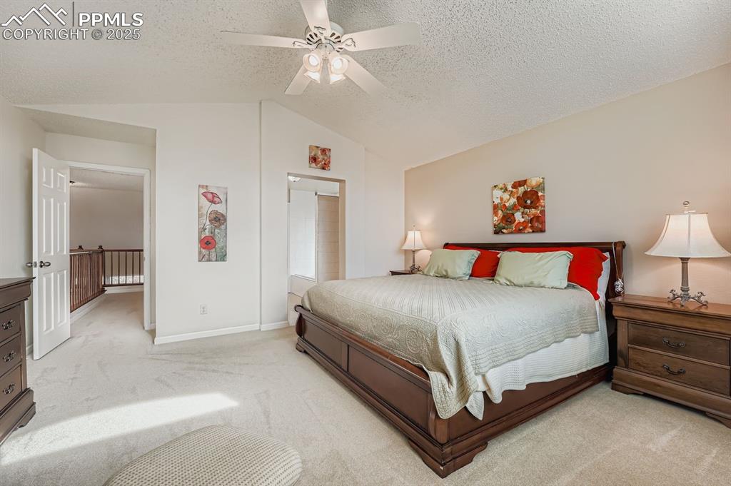 Image 17 of 32: Bedroom with carpet flooring, vaulted ceiling, ceiling fan, and a textured 