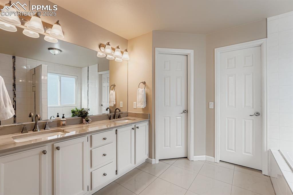 Image 19 of 32: Bathroom with double vanity, light tile patterned floors, tiled shower, and