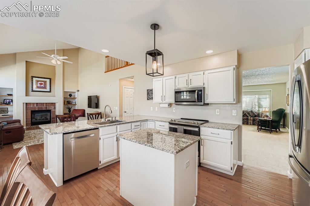 Image 5 of 32: Kitchen with white cabinetry, open floor plan, a peninsula, a fireplace, an