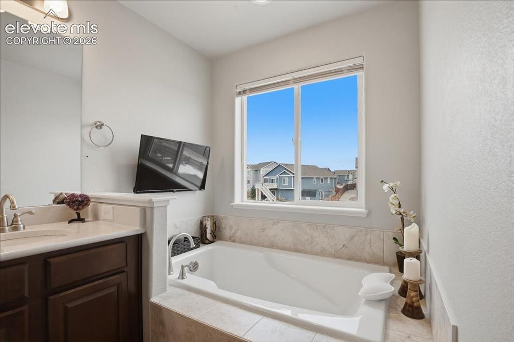 Image 17 of 31: Built-in soaking tub with tile surround, large window, vanity with integrat