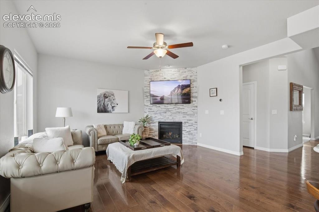 Image 2 of 31: Wood-finish flooring, corner fireplace with stone-look surround, ceiling fa