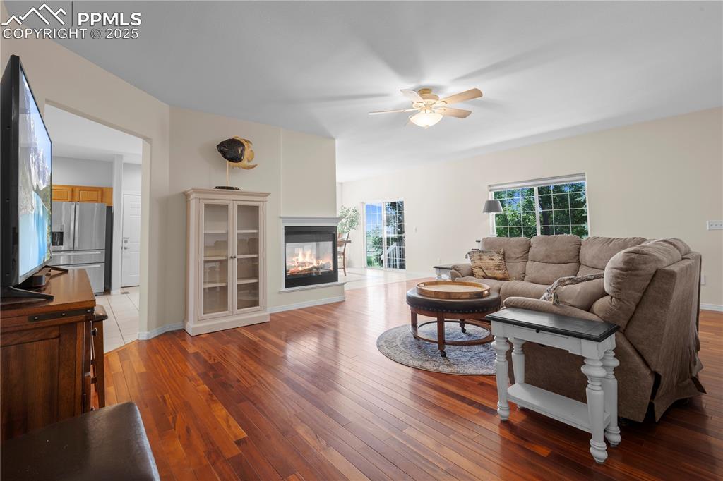 Image 5 of 45: Living room with a ceiling fan, wood-type flooring, and a multi sided firep