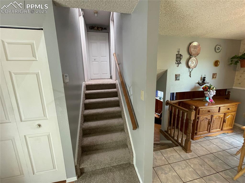 Image 11 of 27: Staircase with a textured ceiling, tile patterned flooring, and baseboards