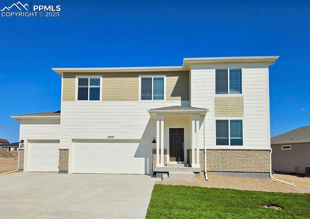 Caption: View of front of house with brick siding, driveway, an attached garage, and a front yard