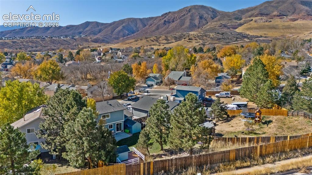Image 2 of 41: Expansive property with a wood privacy fence, mature trees, and a mountain 