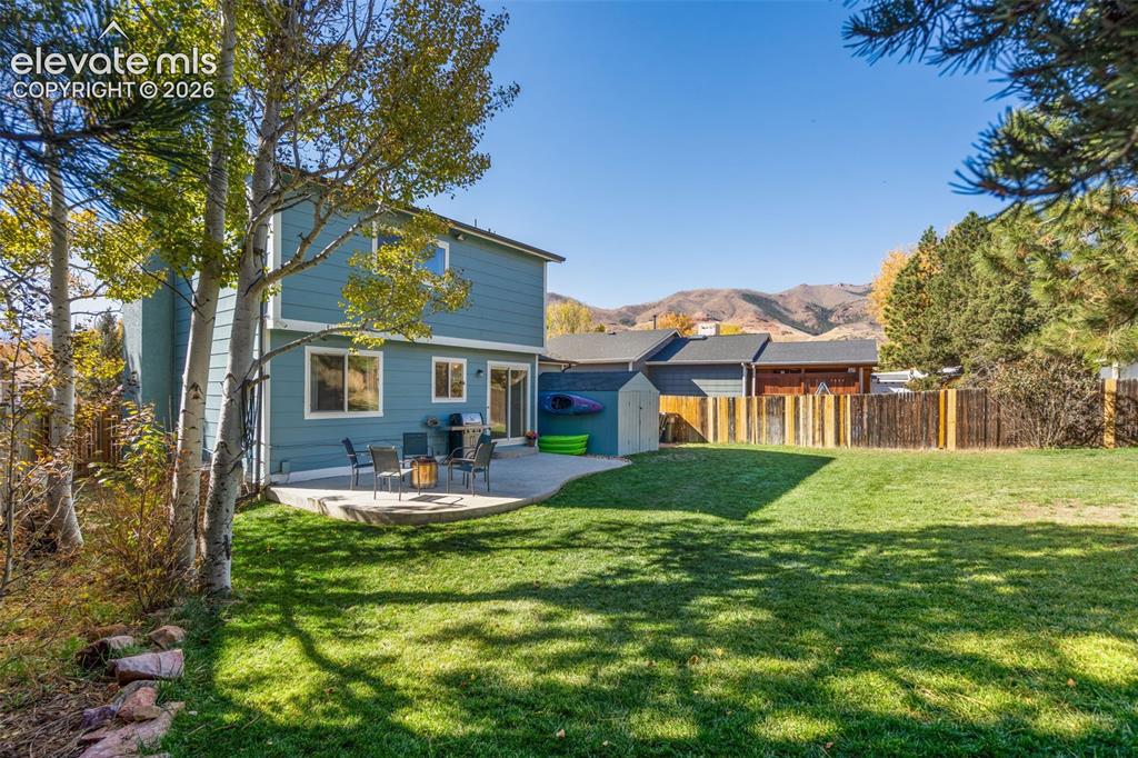 Image 37 of 41: Expansive green lawn with a curved concrete patio, a blue-sided two-story r