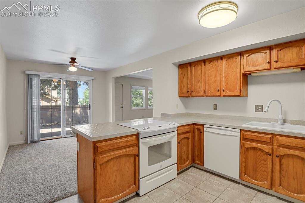 Image 10 of 23: Kitchen with white appliances, a peninsula, brown cabinetry, ceiling fan, a