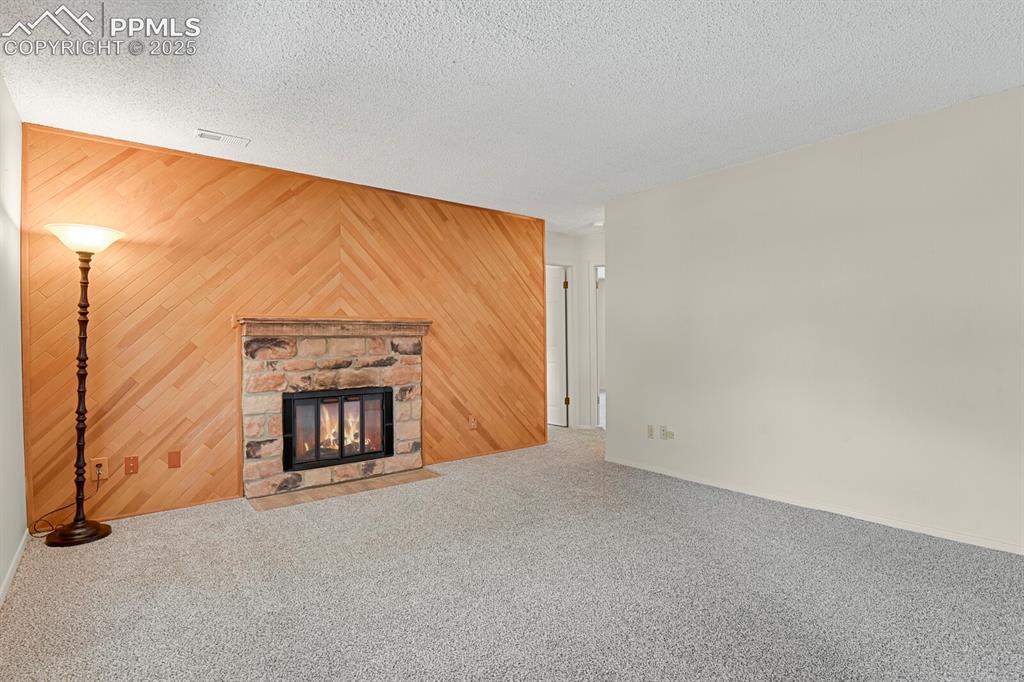 Image 4 of 23: Unfurnished living room featuring wood walls, a fireplace, carpet floors, a