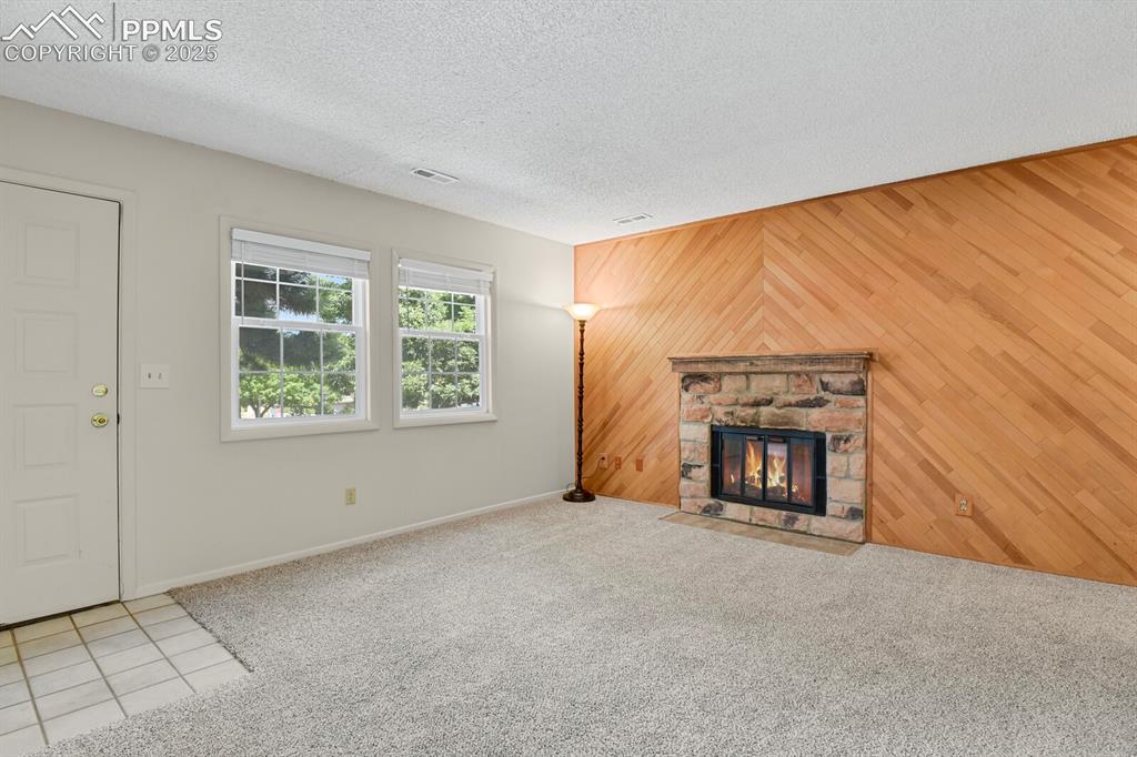 Image 6 of 23: Unfurnished living room featuring wood walls, carpet flooring, a fireplace,