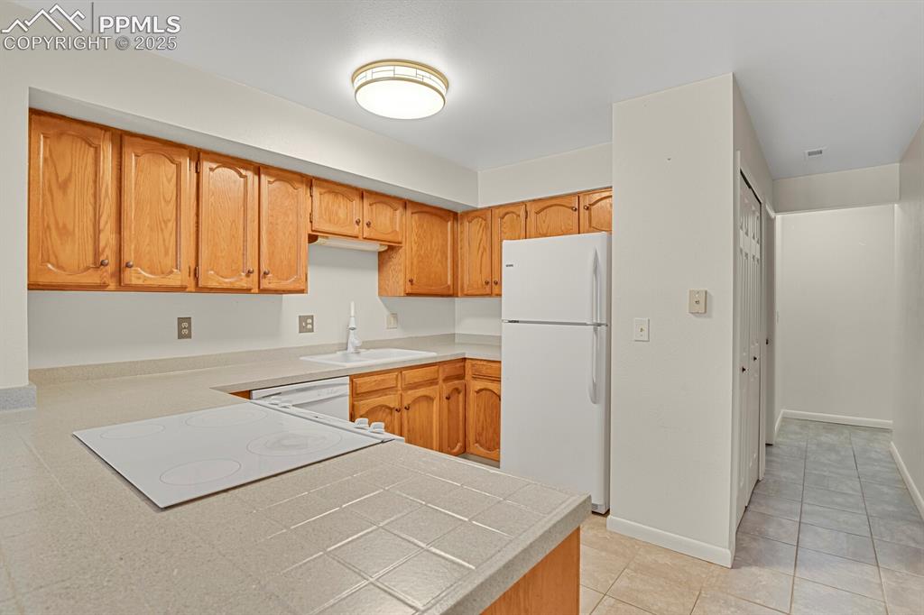 Image 9 of 23: Kitchen featuring white appliances, light tile patterned flooring, tile cou