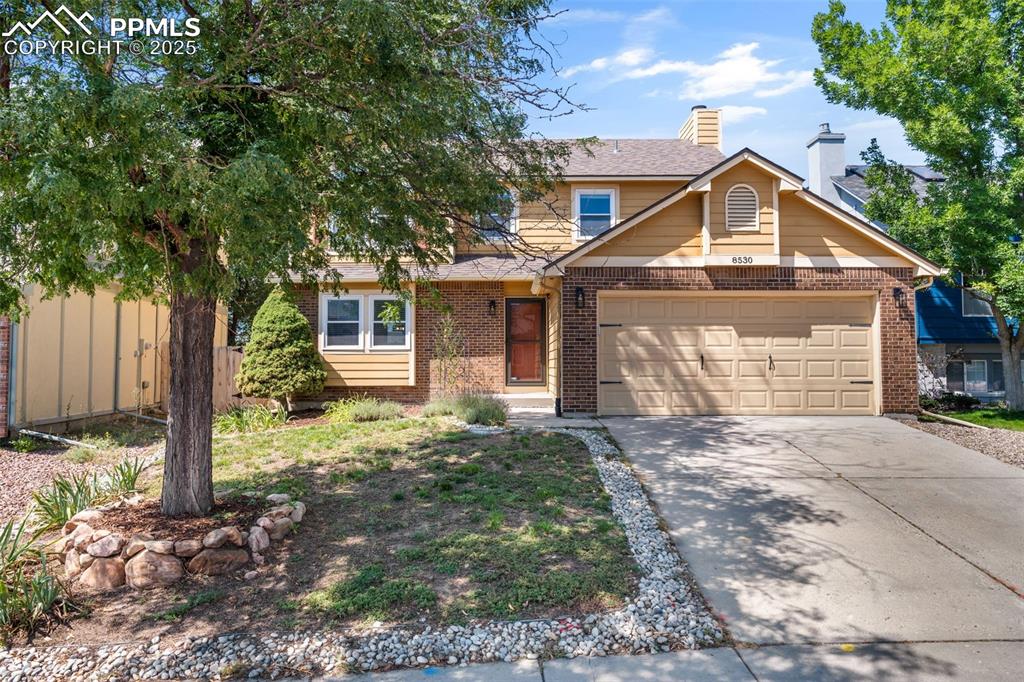 Caption: Traditional-style home featuring brick siding, driveway, a chimney, and an attached garage