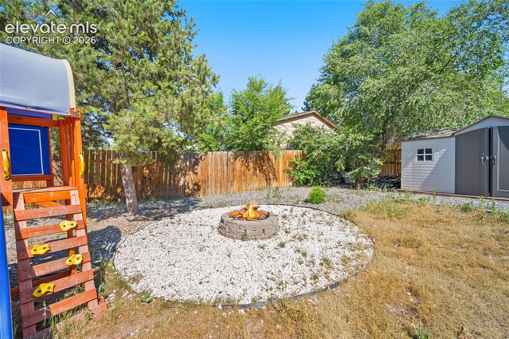 Image 38 of 50: Backyard with fire pit, play area, and storage shed.