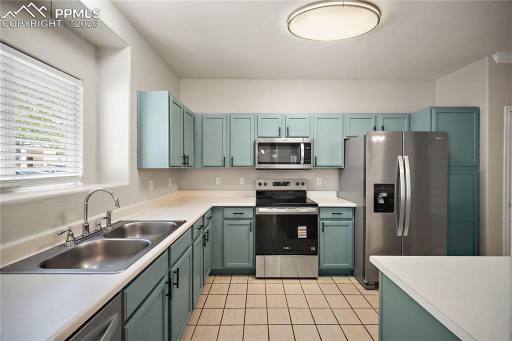 Image 13 of 31: Kitchen featuring teal cabinetry with black hardware, light countertops, st