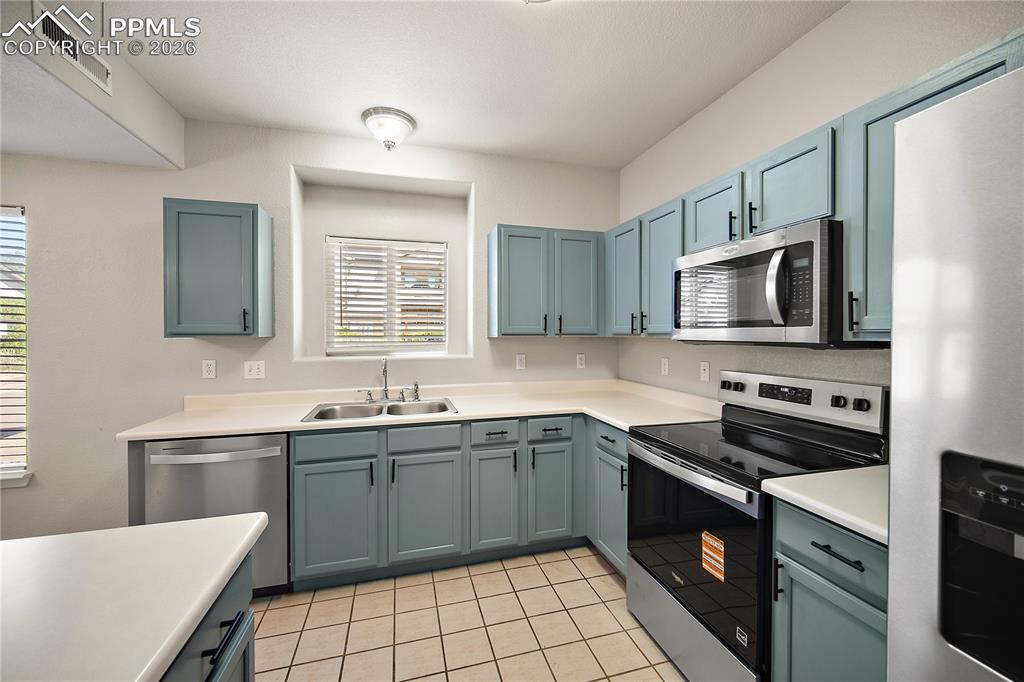 Image 15 of 31: Kitchen featuring teal cabinetry, stainless steel appliances, white counter