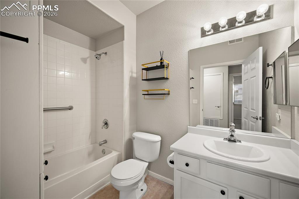 Image 25 of 31: Bathroom featuring a white bathtub with tile surround, white toilet, and a 