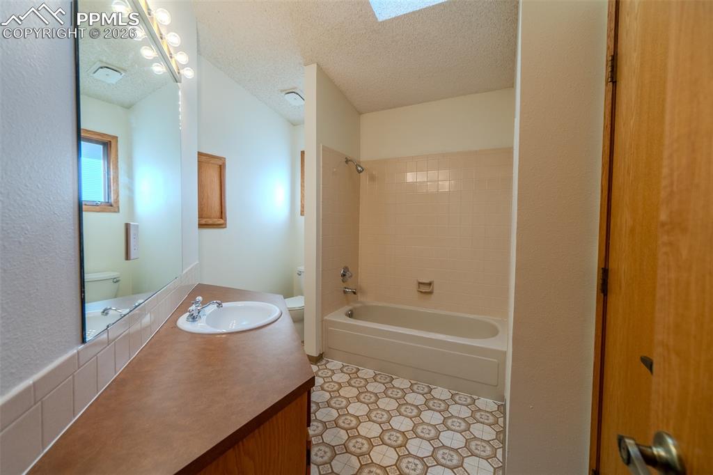Image 9 of 26: Full bath with vanity, a textured ceiling, bathing tub / shower combination