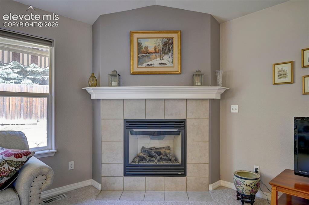 Image 21 of 50: Gas fireplace with tile surround and wood mantle in living area.